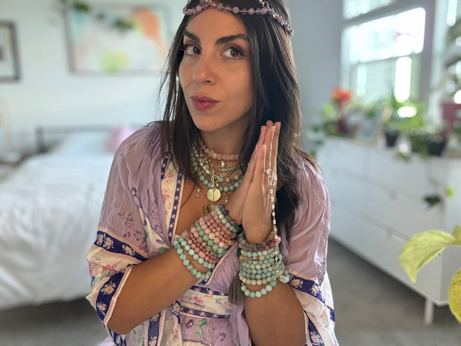 Woman in a room with a blurred background, wearing a patterned outfit and multiple necklaces.